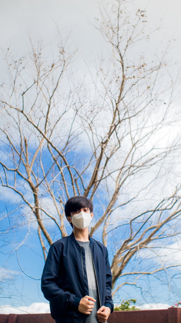 Portrait of a young man wearing a face mask with a leafless tree in the background, symbolizing safety and seasonal transition.