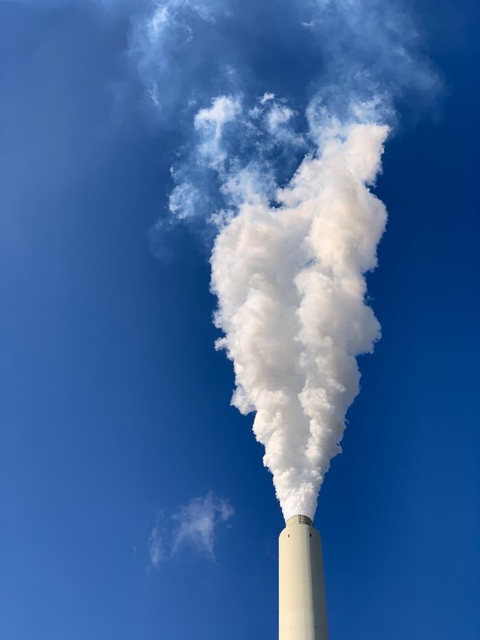 Vertical shot of a factory smokestack releasing white smoke on a clear day in Karlsruhe, Germany.