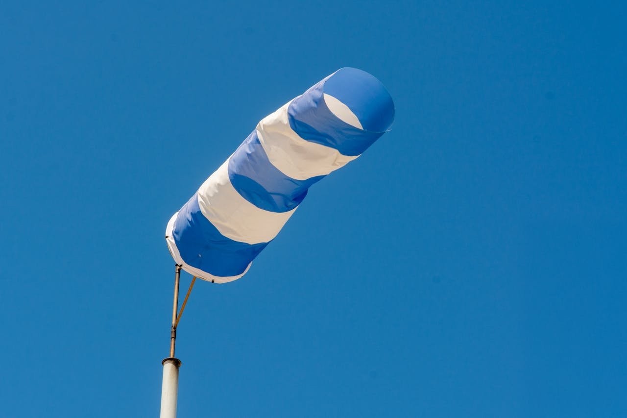 A blue and white windsock blowing in the wind against a clear blue sky.