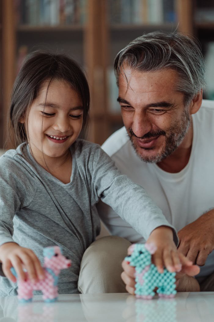 A father and daughter enjoy playing with colorful toy figures indoors, smiling warmly.