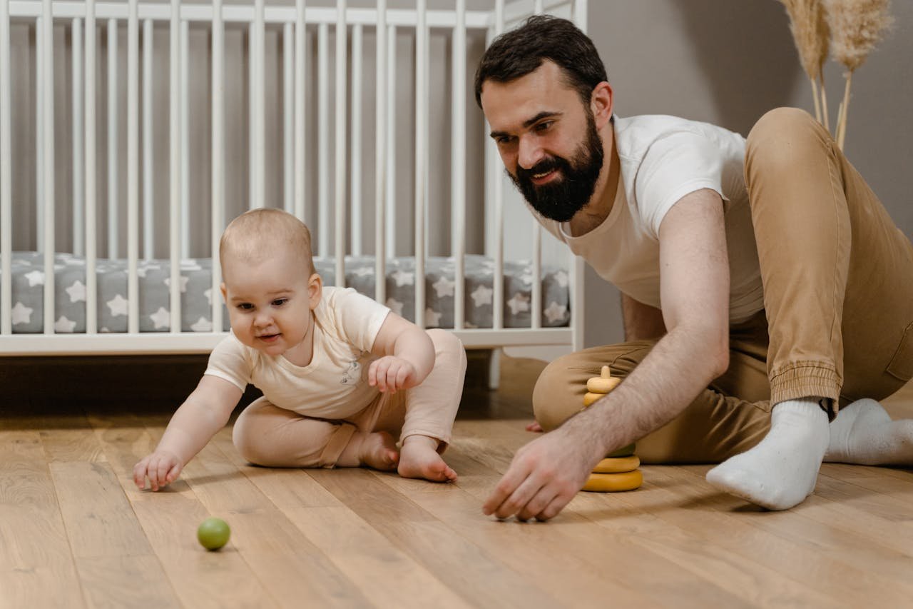 Father bonding with his baby in a cozy nursery, enjoying quality playtime on a wooden floor.